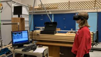 person in red sweater wearing a VR headset in a lab in front of a computer